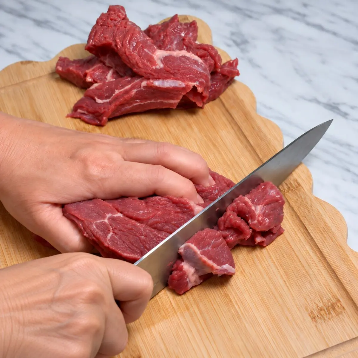 Mary cutting beef chuck into pieces on a wooden cutting board.