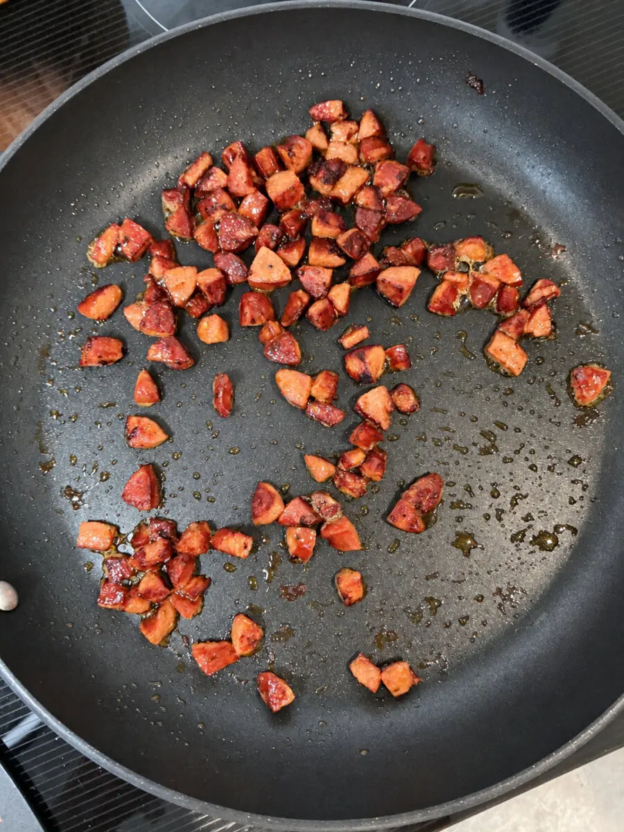 Diced andouille sausage browning in a black skillet.