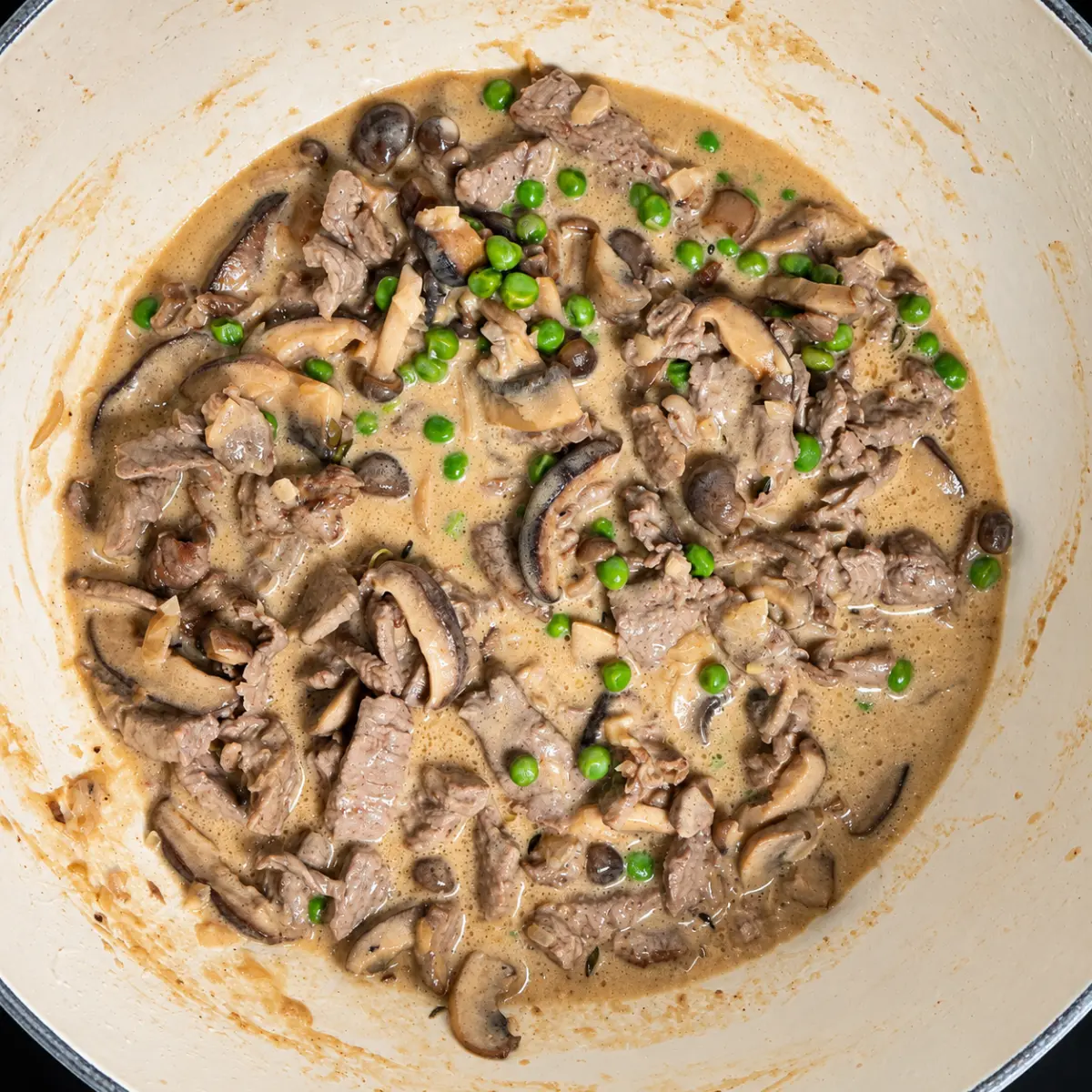 Beef stroganoff with mushrooms and green peas in a creamy sauce in an enameled skillet.