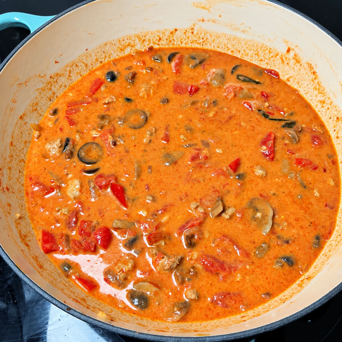 Butter Chicken Riggies cream sauce with chicken, mushrooms, peppers and olives in a turquoise pan.