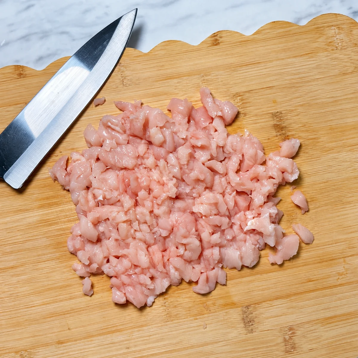 Raw chicken chopped on a wooden cutting board beside a knife.